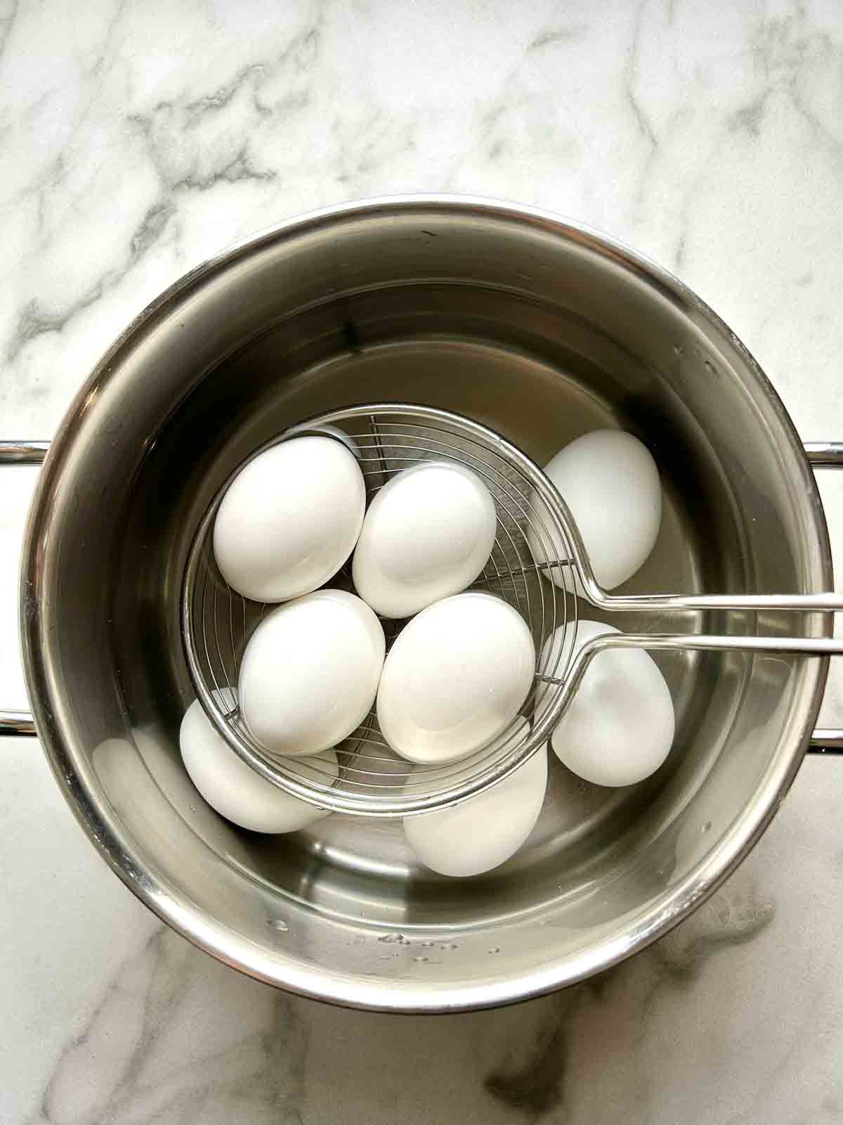 eggs boiling in water with metal spider scooping some of them