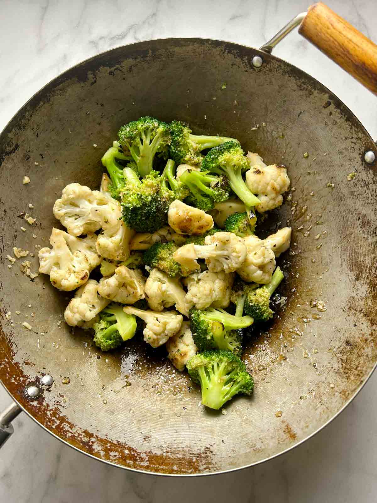 broccoli and cauliflower tossed with sauce in wok.