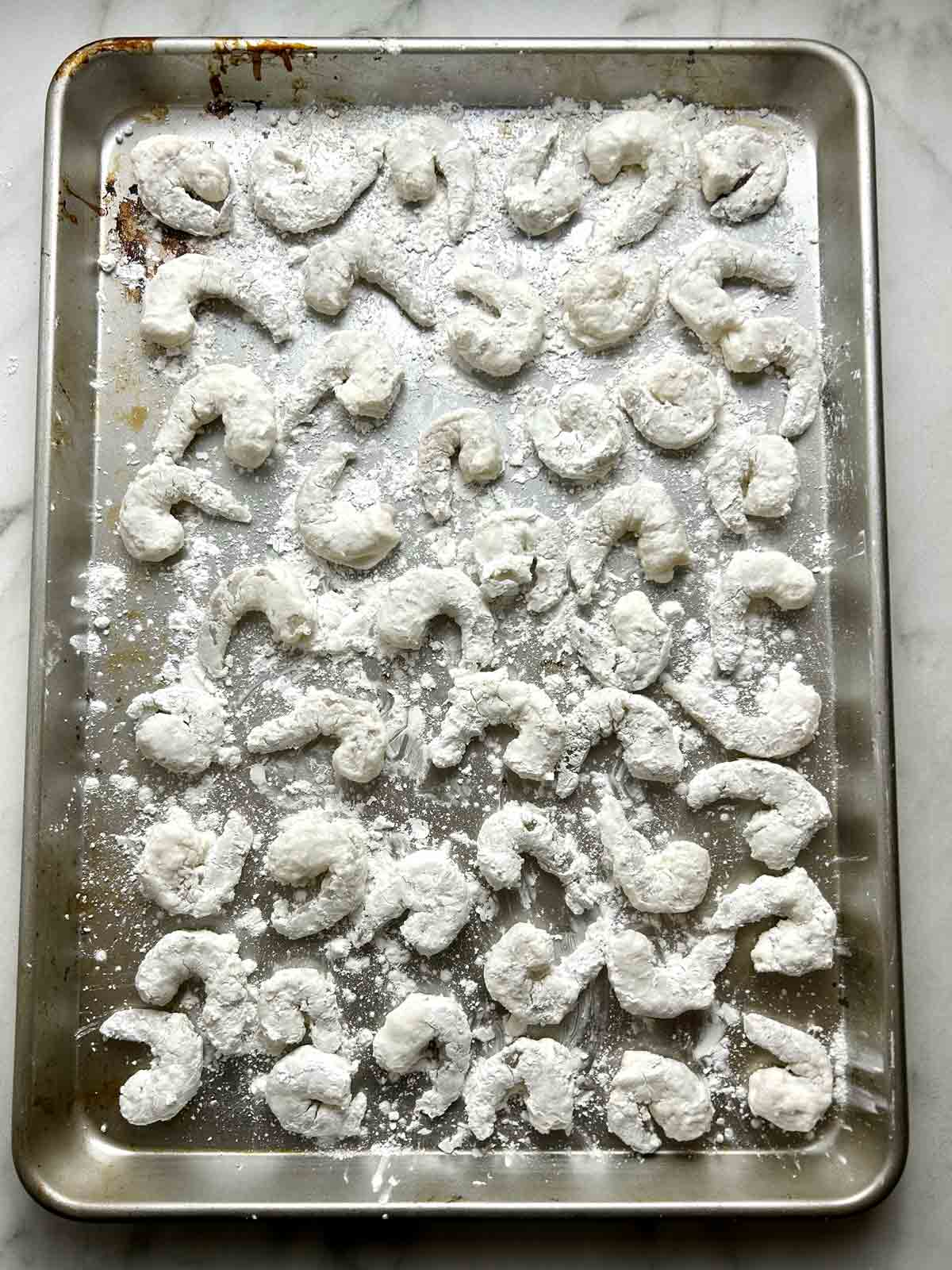 coated shrimps resting on baking sheet.