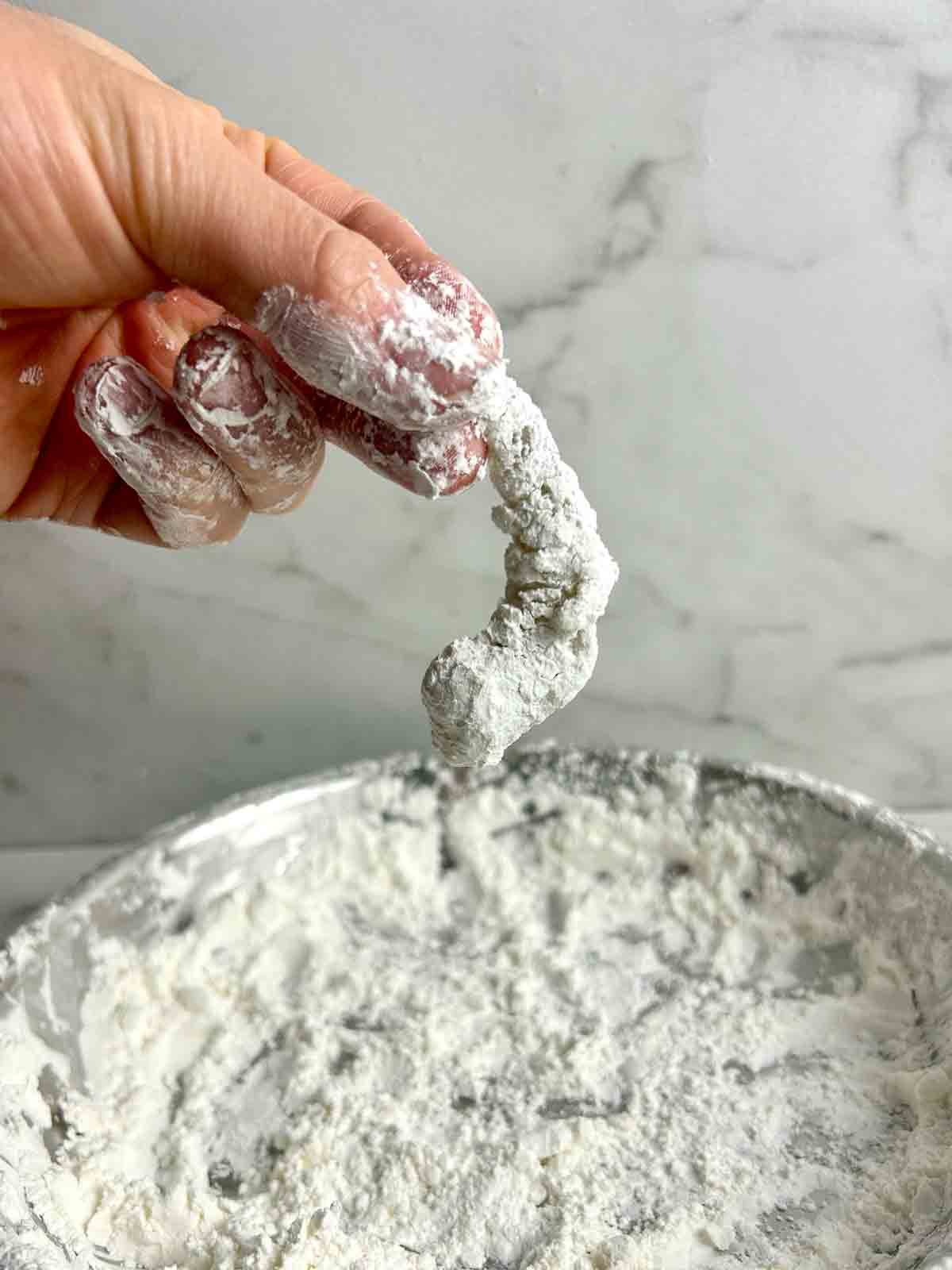 hand holding shrimp coated in cornstarch mixture.