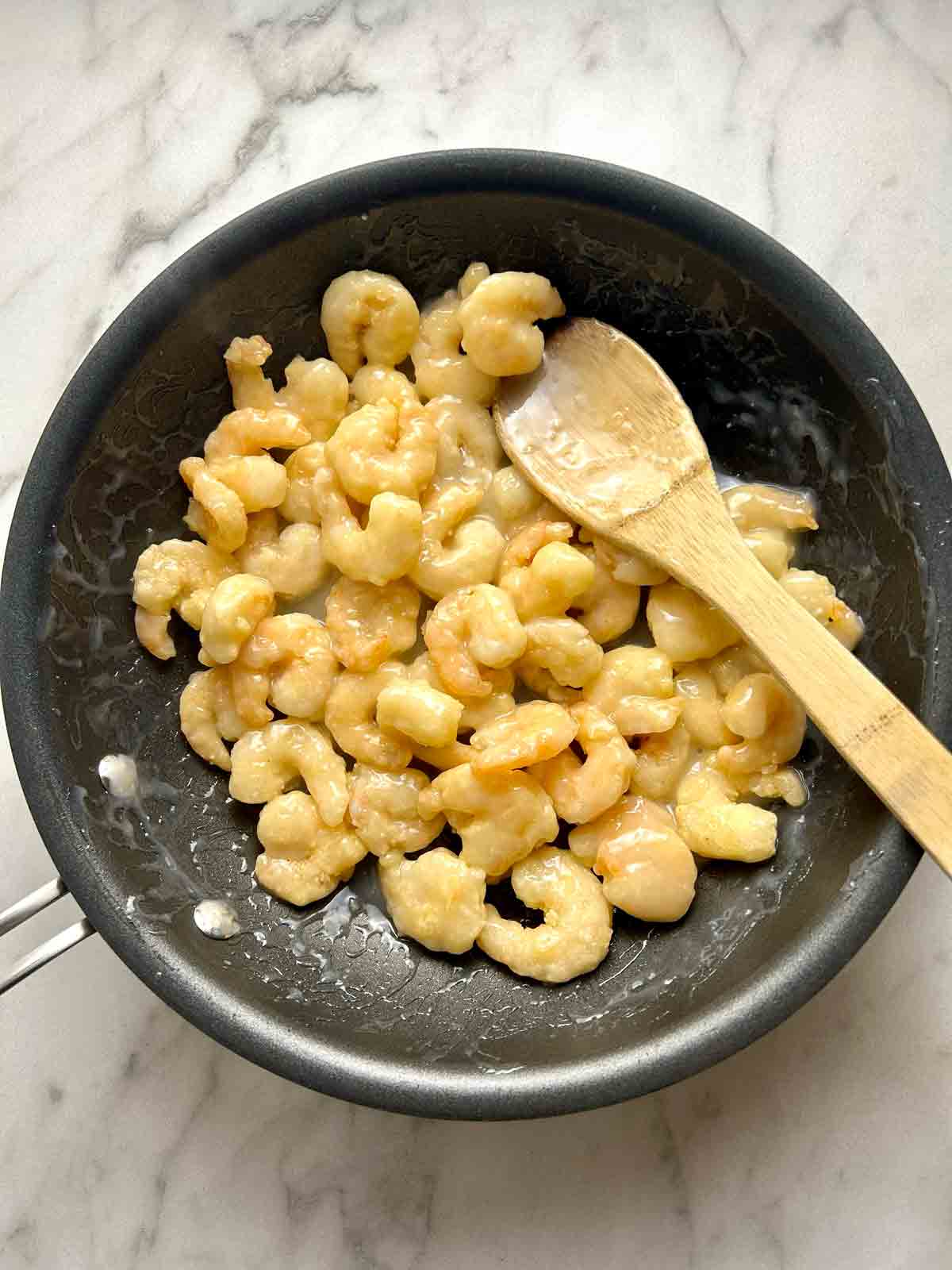 fried shrimp being coated in coconut sauce.