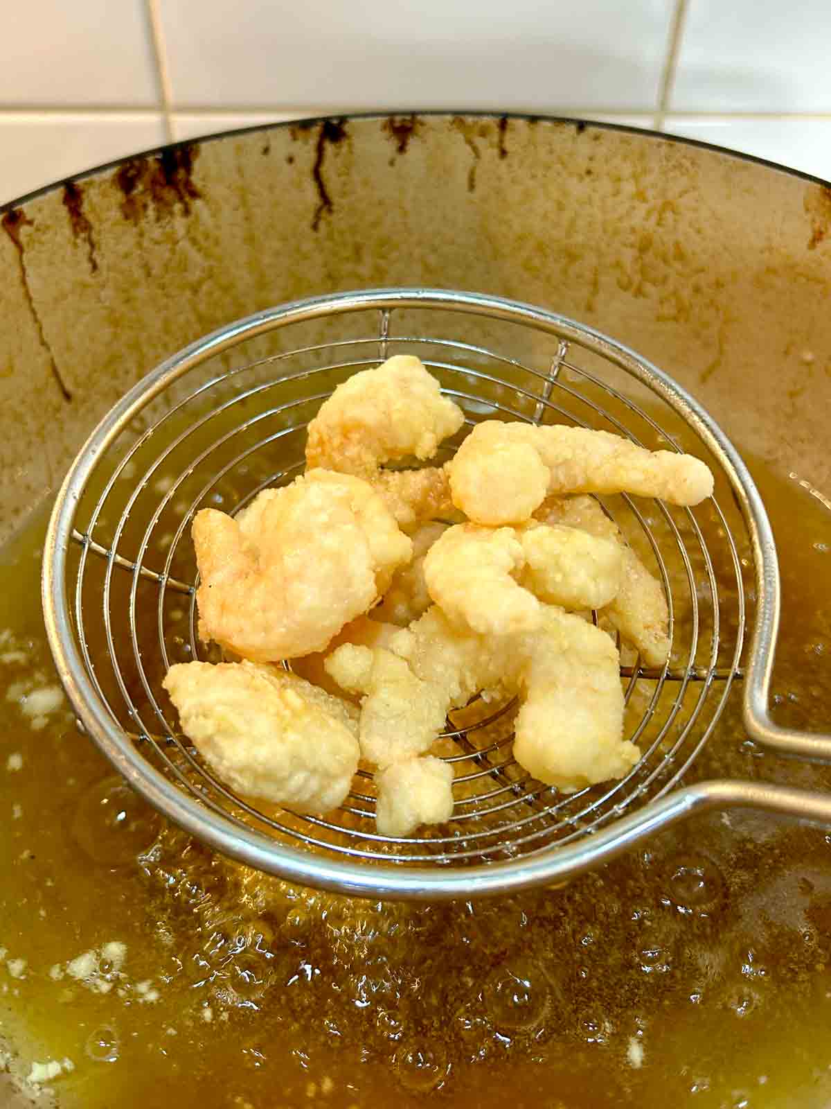 metal spider scooping out fried shrimp from hot oil.