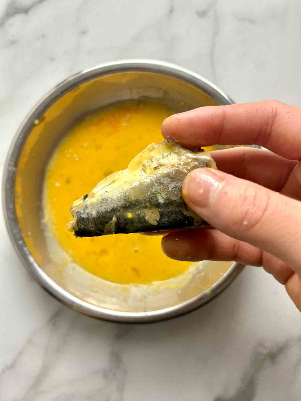 sardine being coated in egg wash.