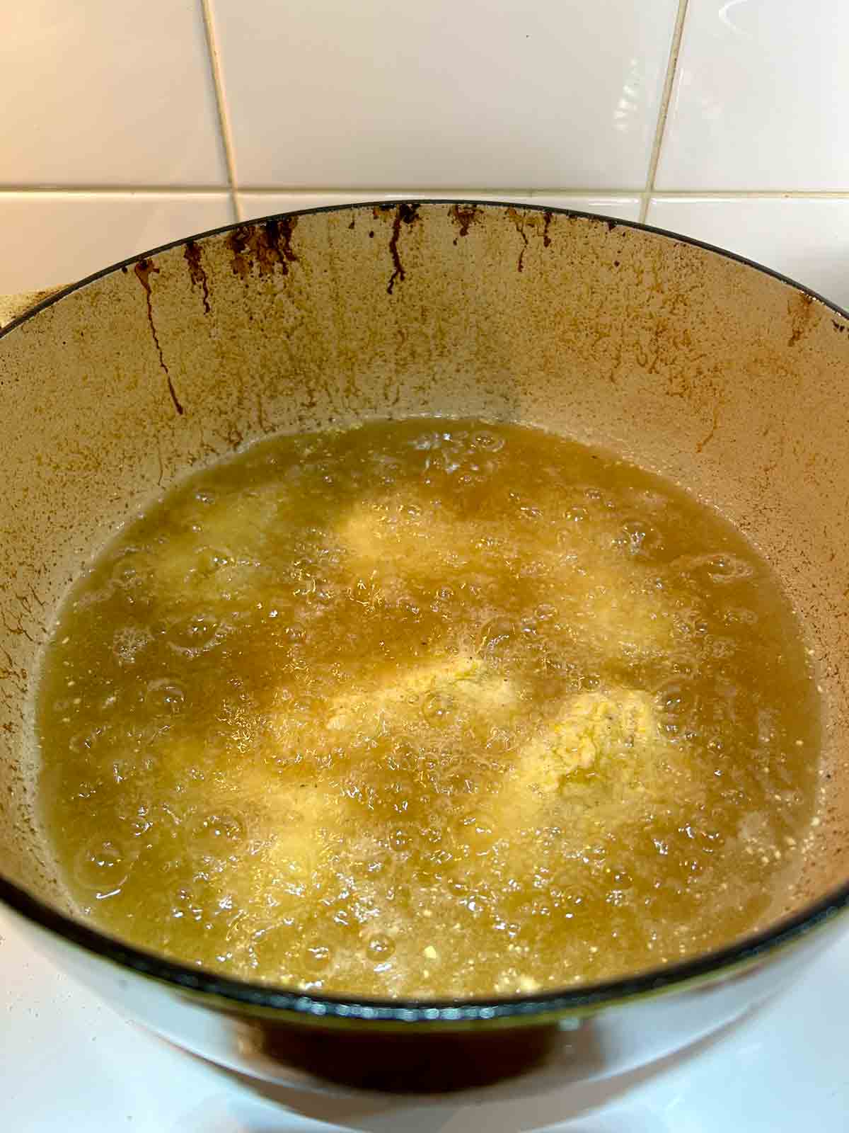 breaded sardines being fried in hot oil in Dutch oven.