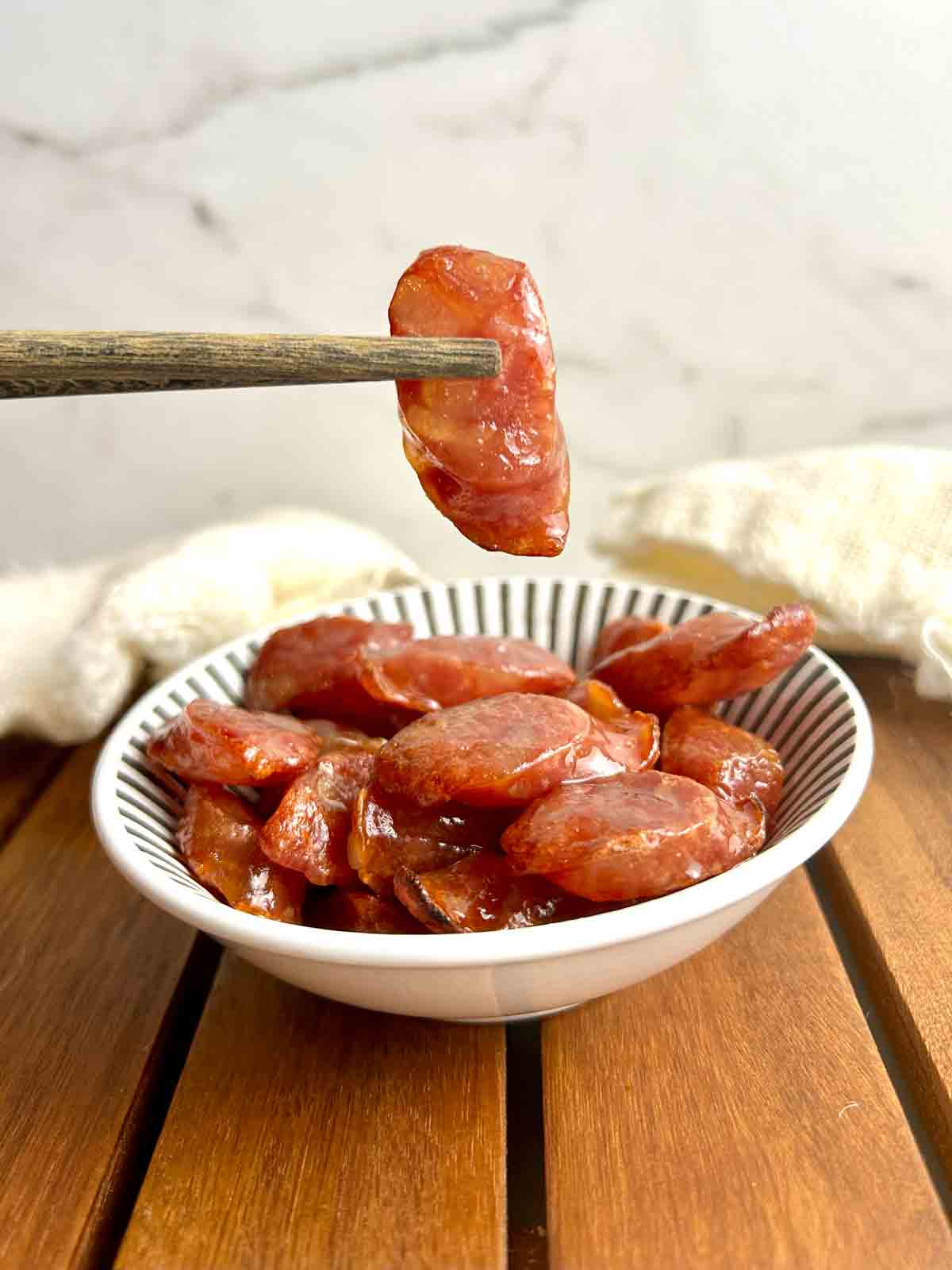 chopsticks holding sliced of air-fried Chinese sausage