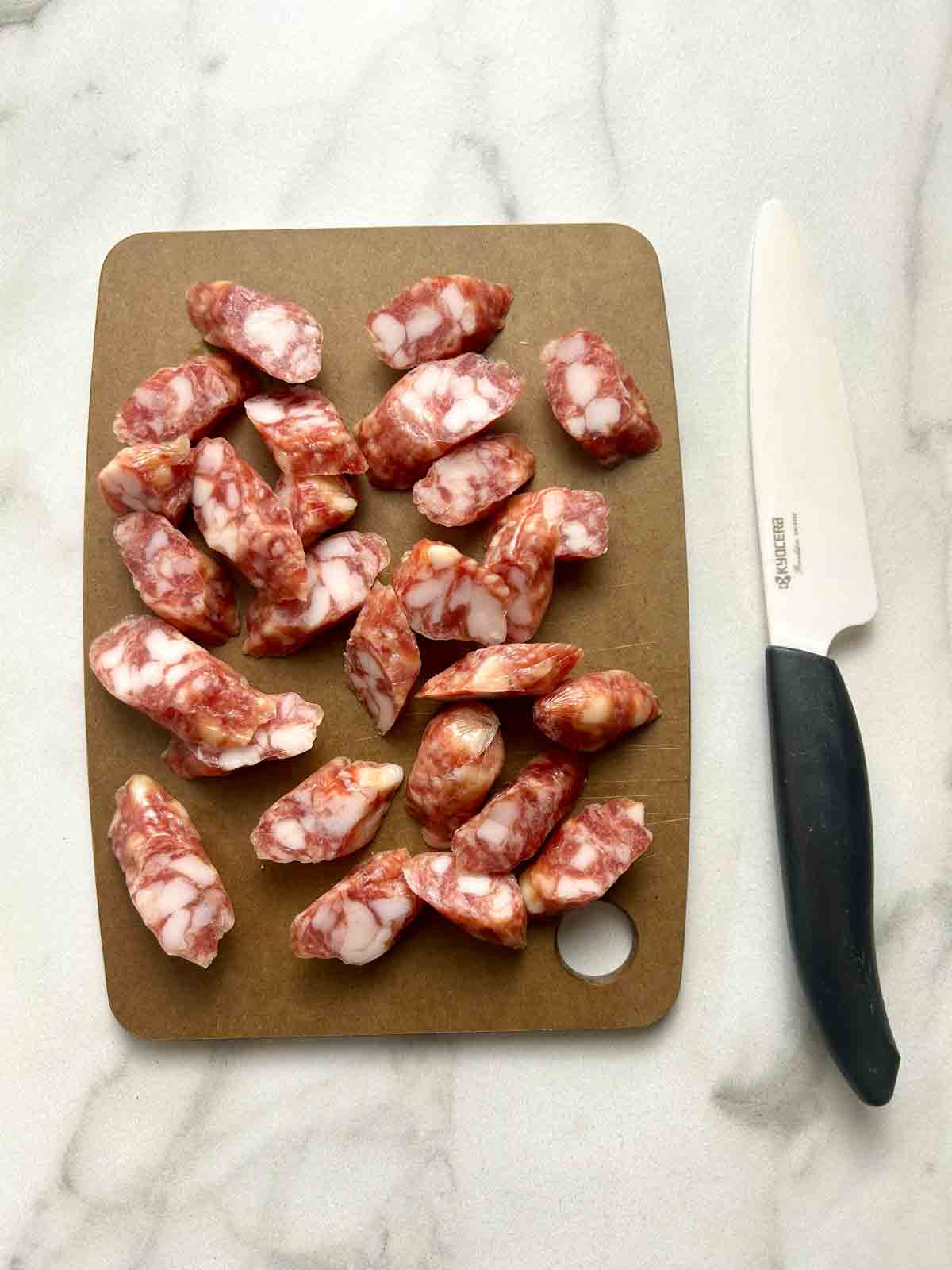 Chinese sausage sliced into pieces on wooden cutting board.