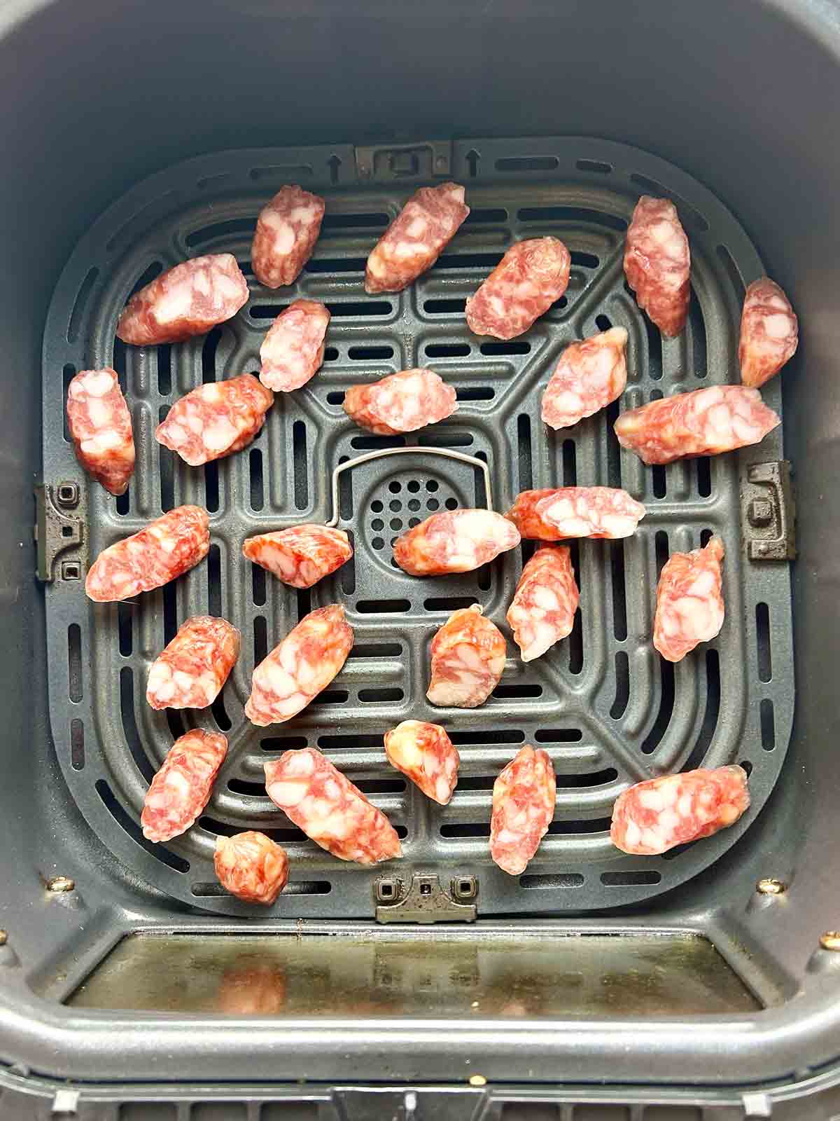 sliced Chinese sausages in air-fryer basket before cooking.