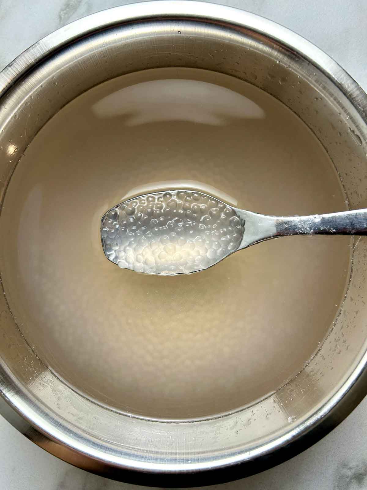 cooked tapioca pearls being lifted out fo water with spoon.