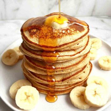 syrup being drizzled onto plate of banana oatmeal pancakes.