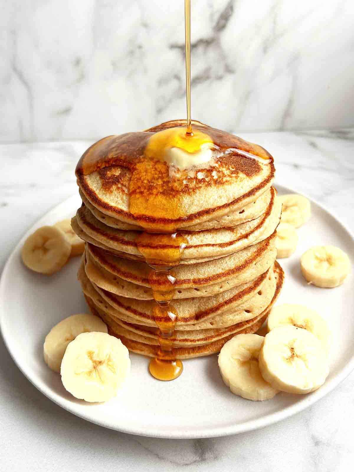 syrup being drizzled onto plate of banana oatmeal pancakes.