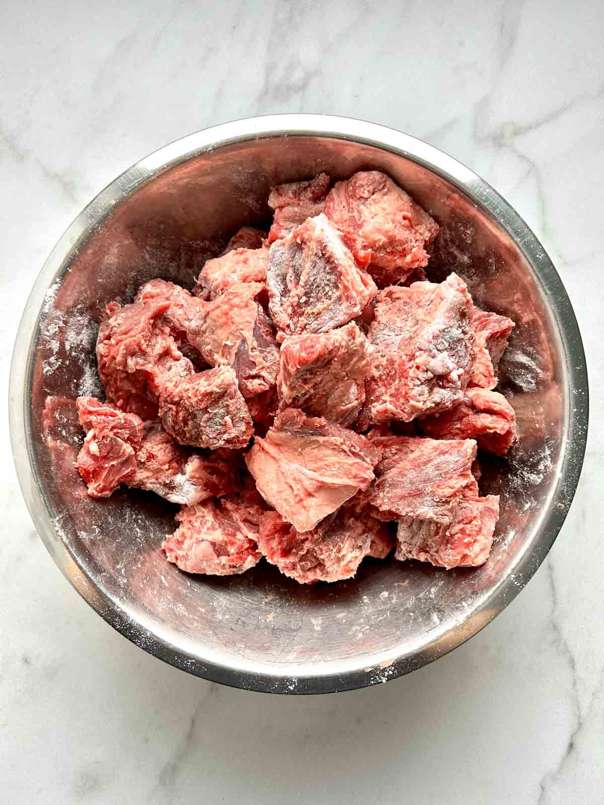 beef cubes tossed with flour in bowl.