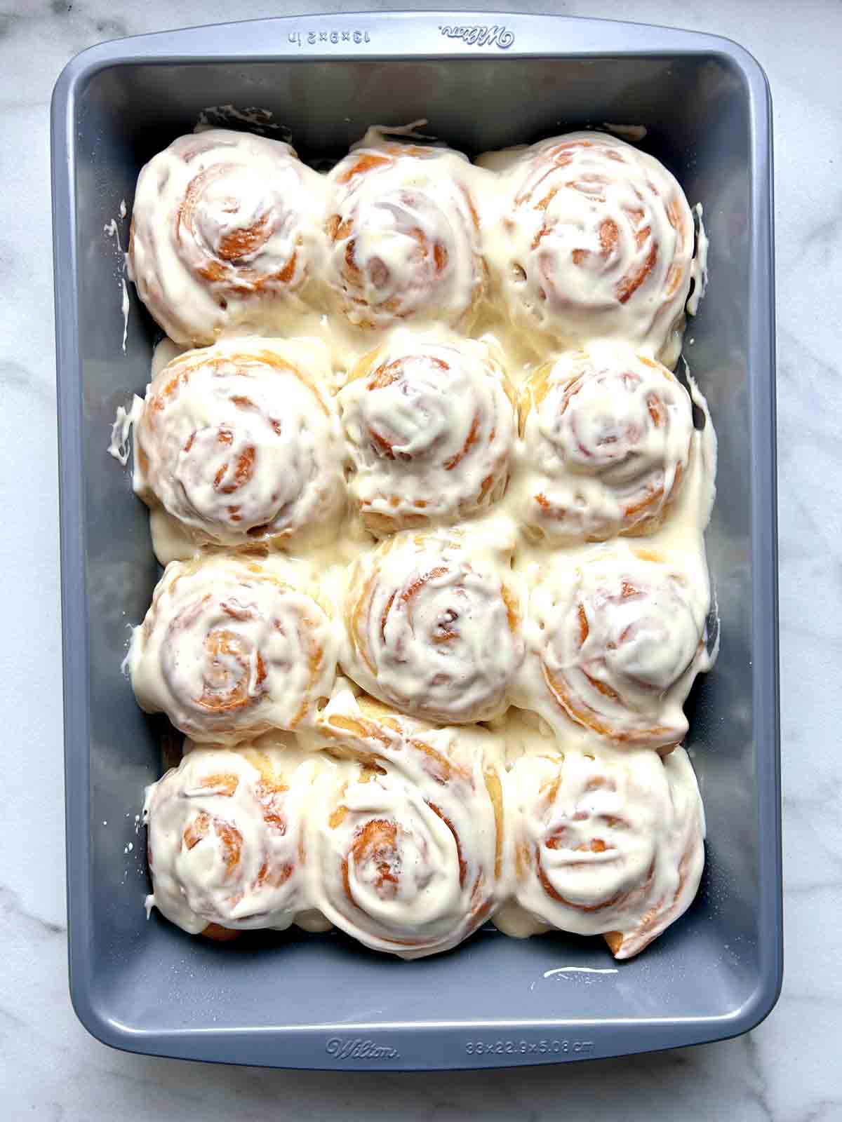 cinnamon rolls covered in icing in balking pan.