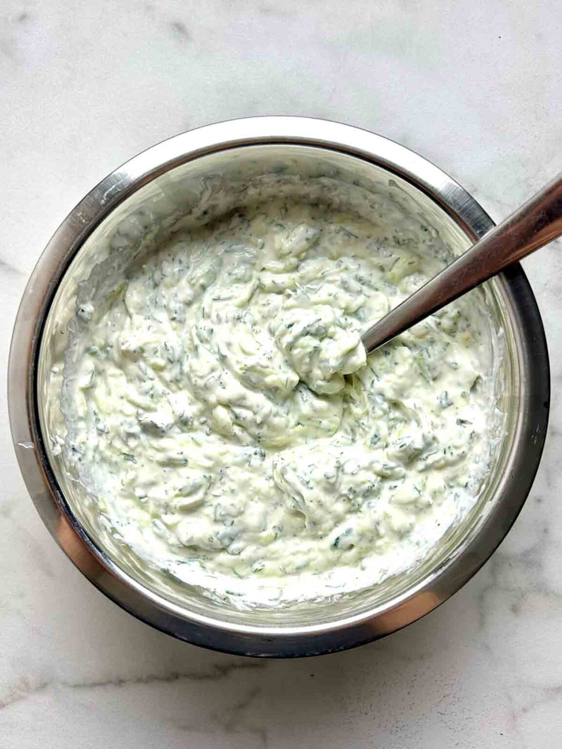 Mixing ingredients for tzatziki in a large glass bowl