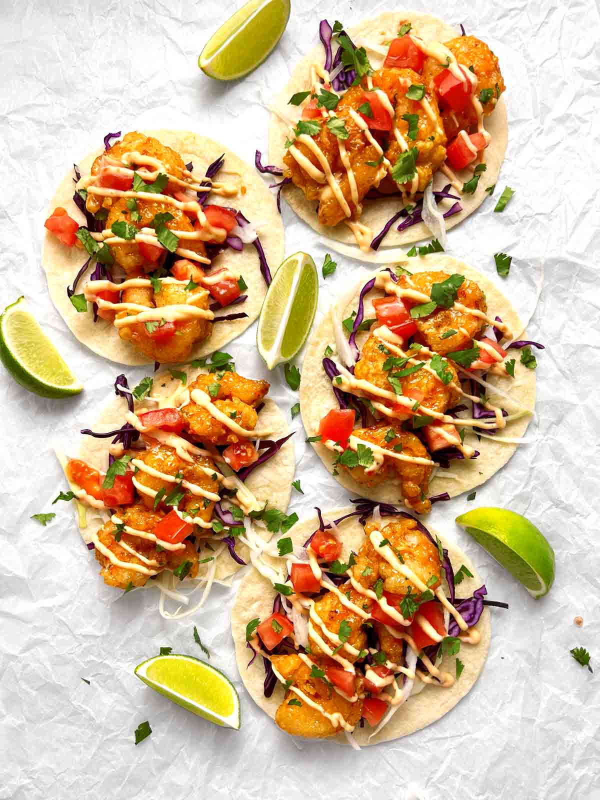 close up of assembled bang bang shrimp tacos on parchment paper.