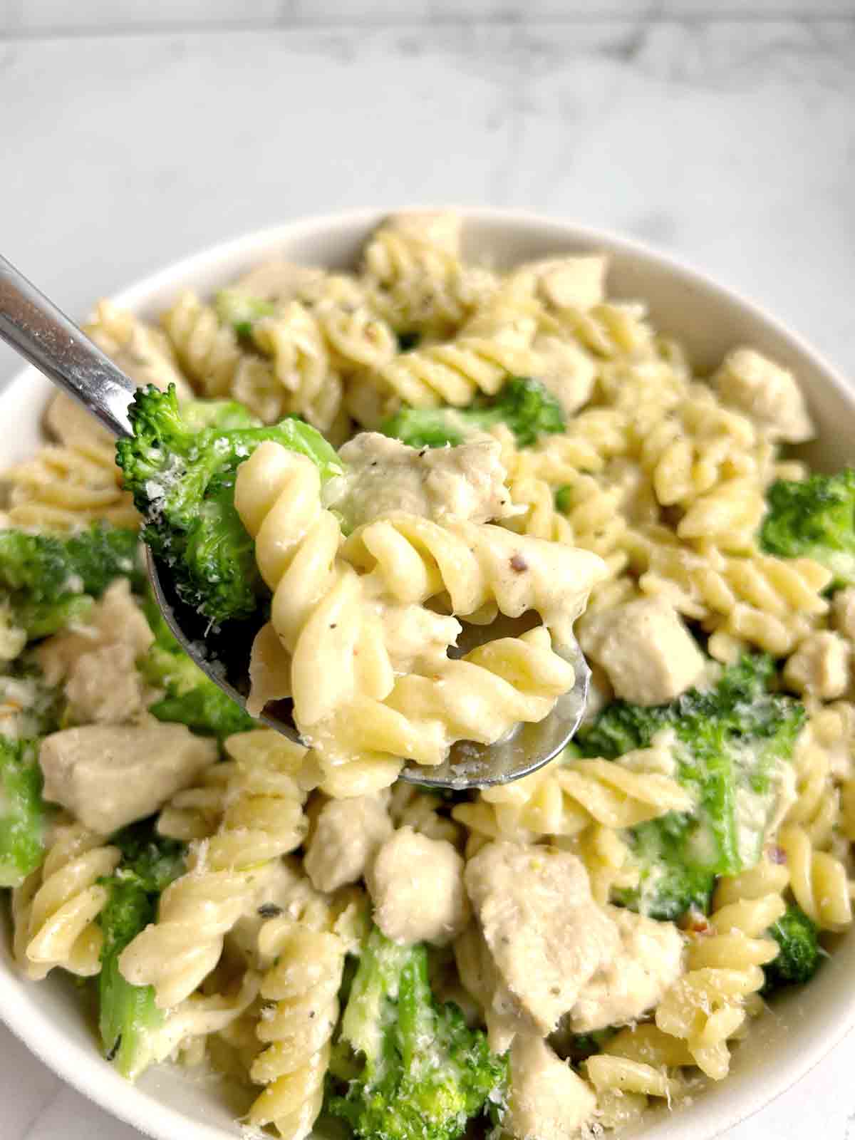 spoon lifting chicken and broccoli pasta from plate.