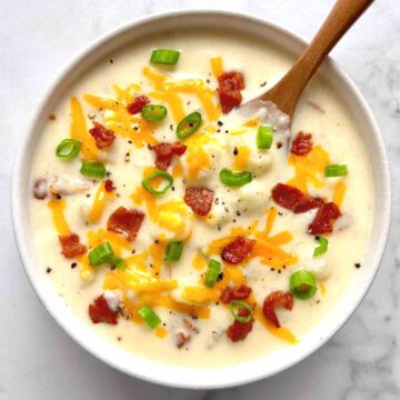 bowl of potato soup with cheddar cheese, green onions, and bacon sprinkled on top.