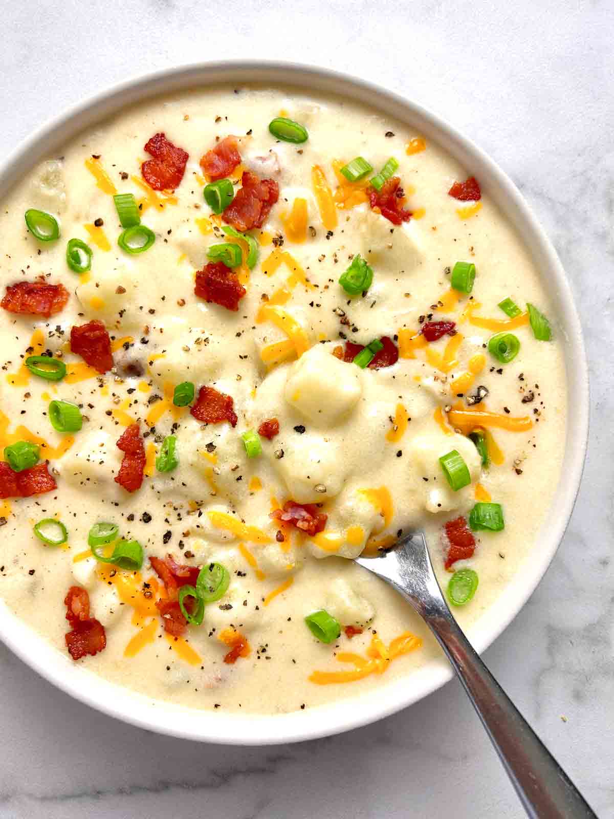 overhead shot of bowl of potato soup with garnishes on top.