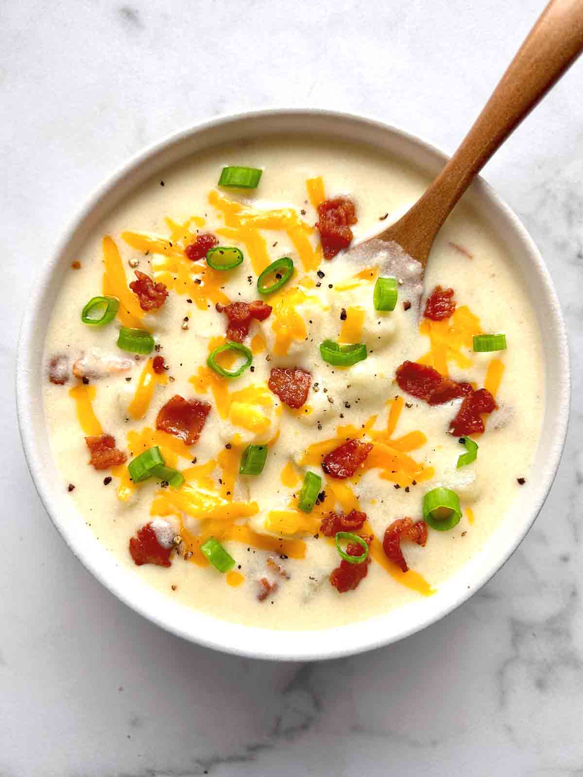 bowl of potato soup with cheddar cheese, green onions, and bacon sprinkled on top.