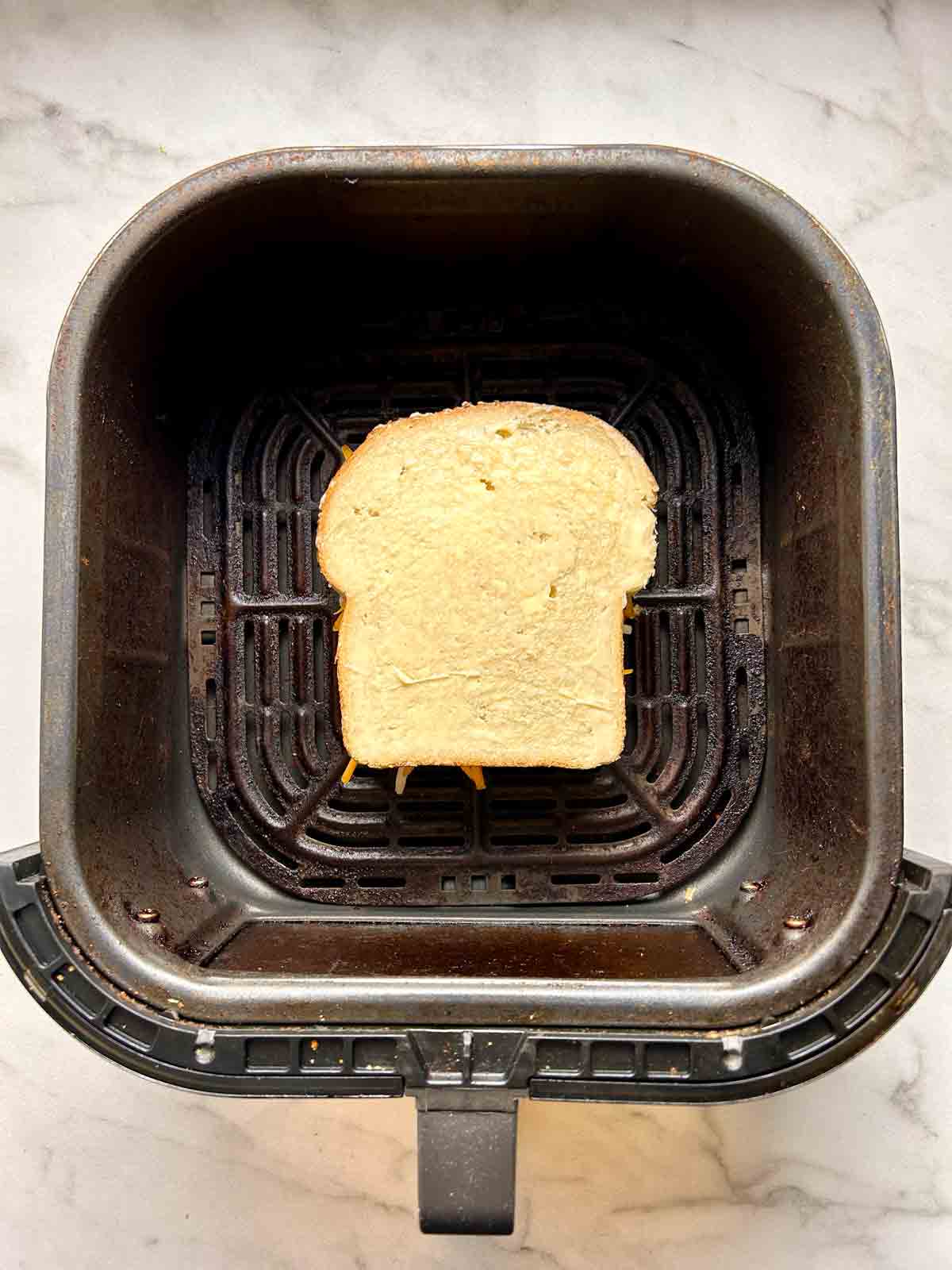 uncooked, completed sandwich sitting in air fryer basket.