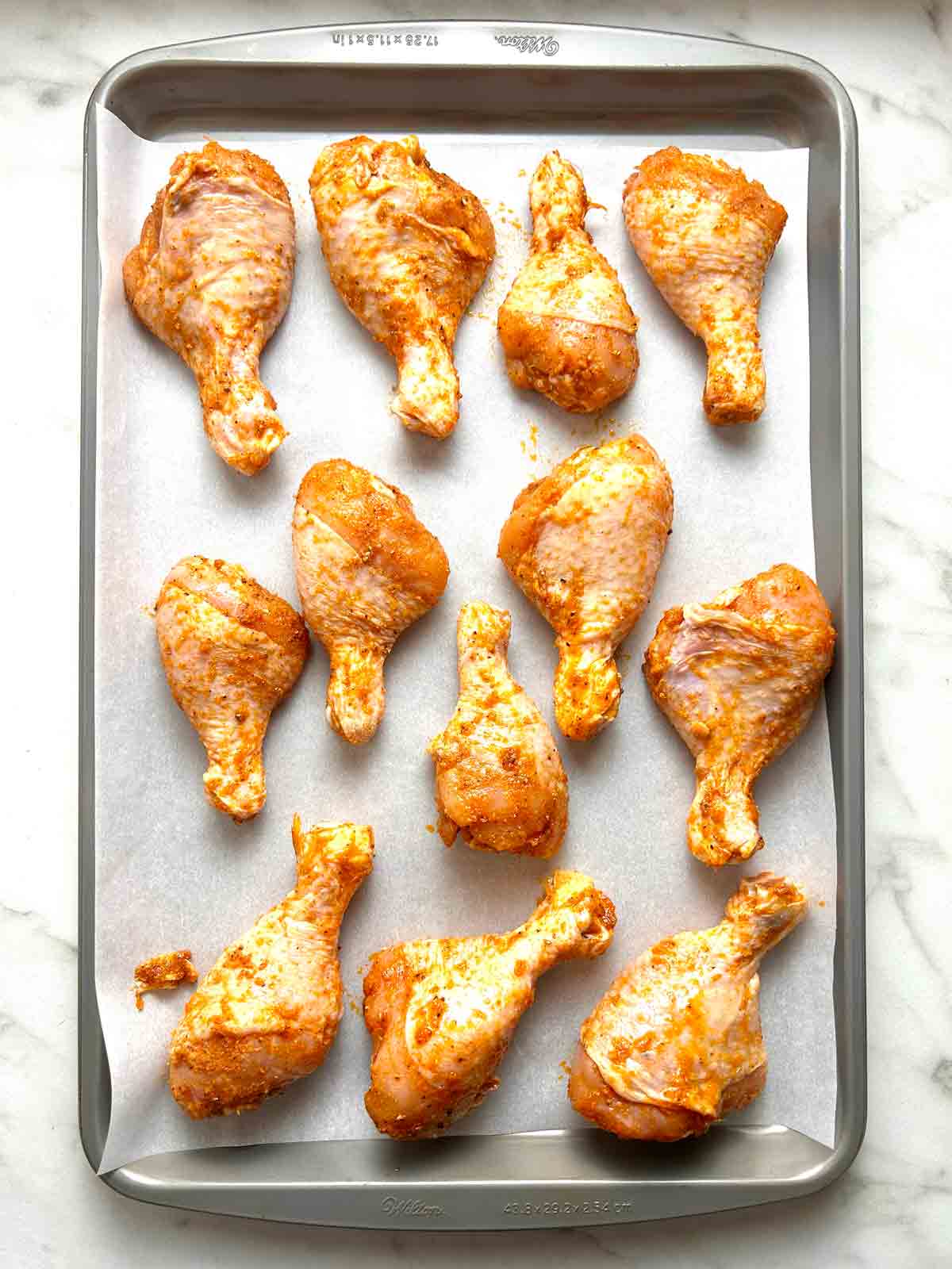seasoned chicken legs on parchment-lined baking sheet.