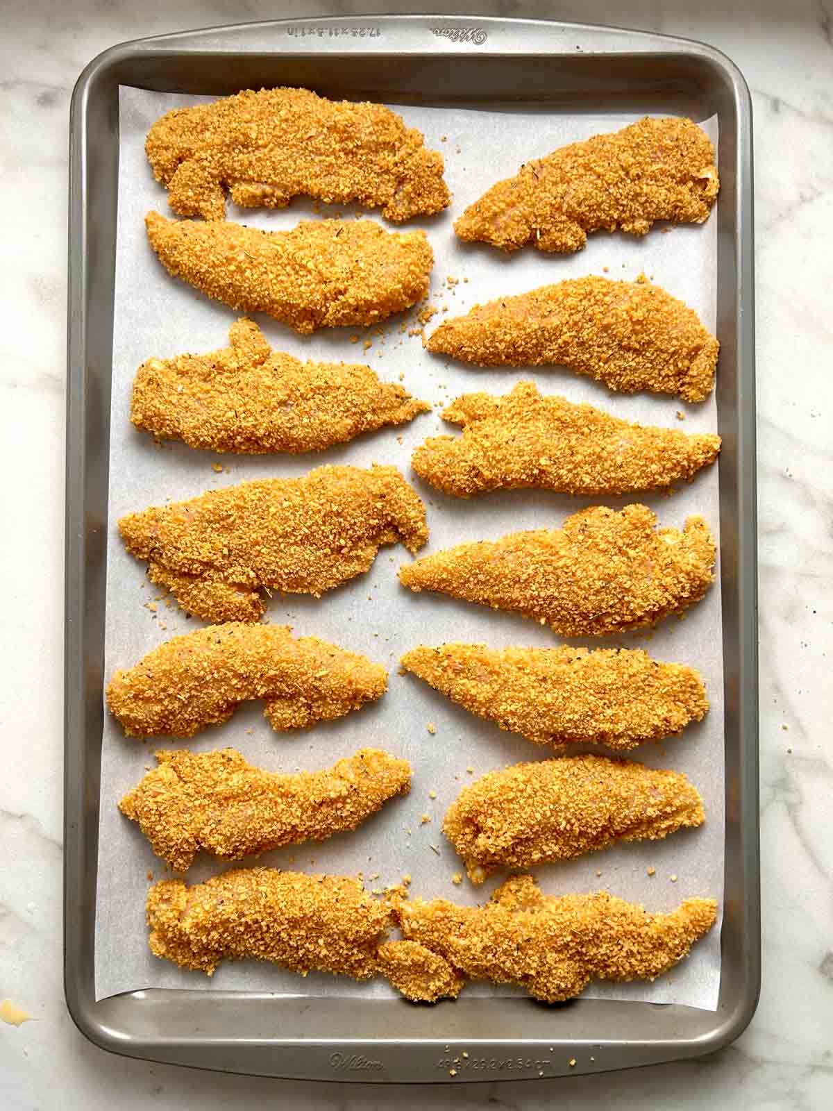 breaded chicken tenders on baking sheet.