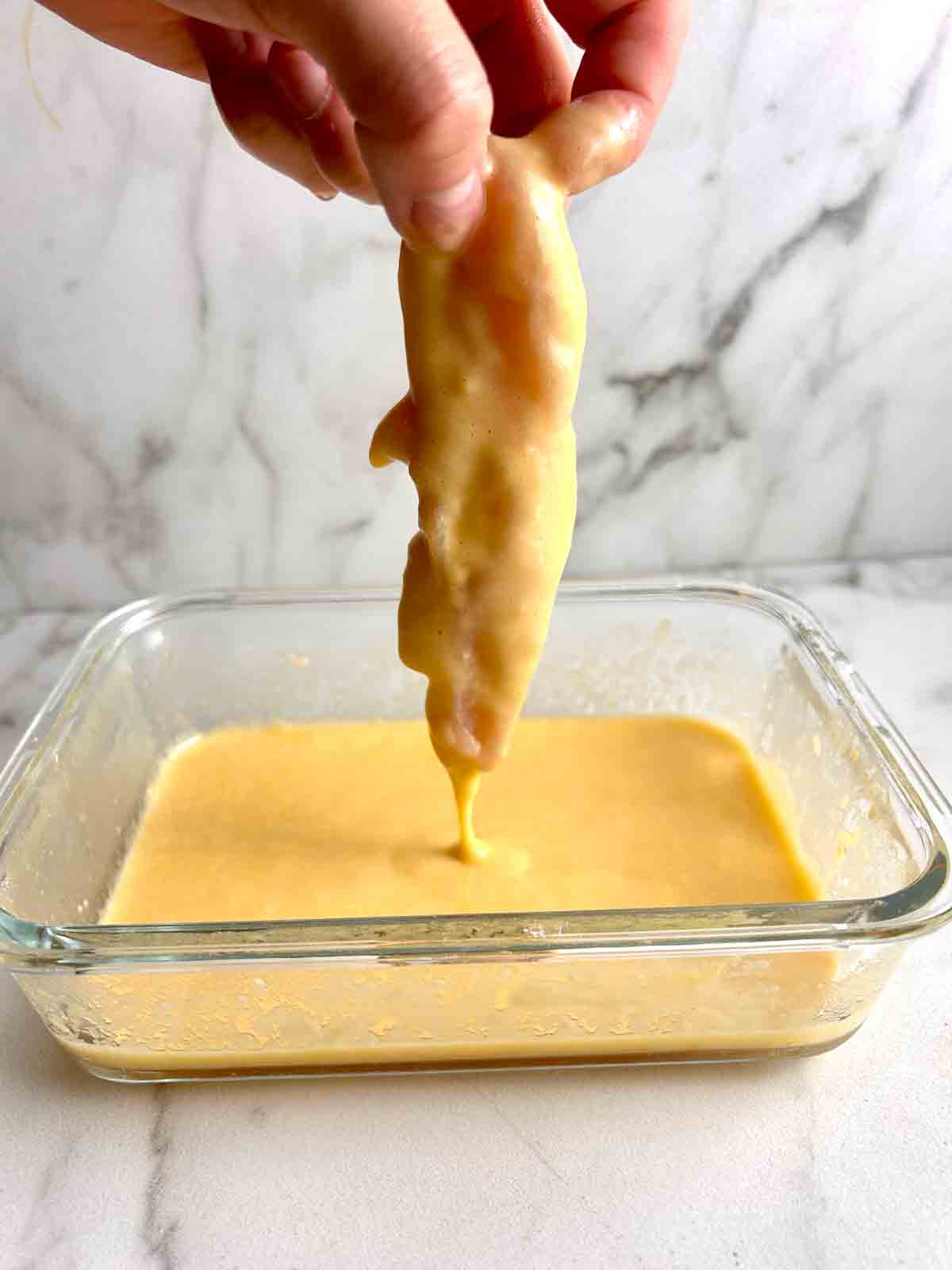 dredging chicken tender in egg wash.