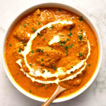 bowl of butter chicken with parsley and cream garnished on top.