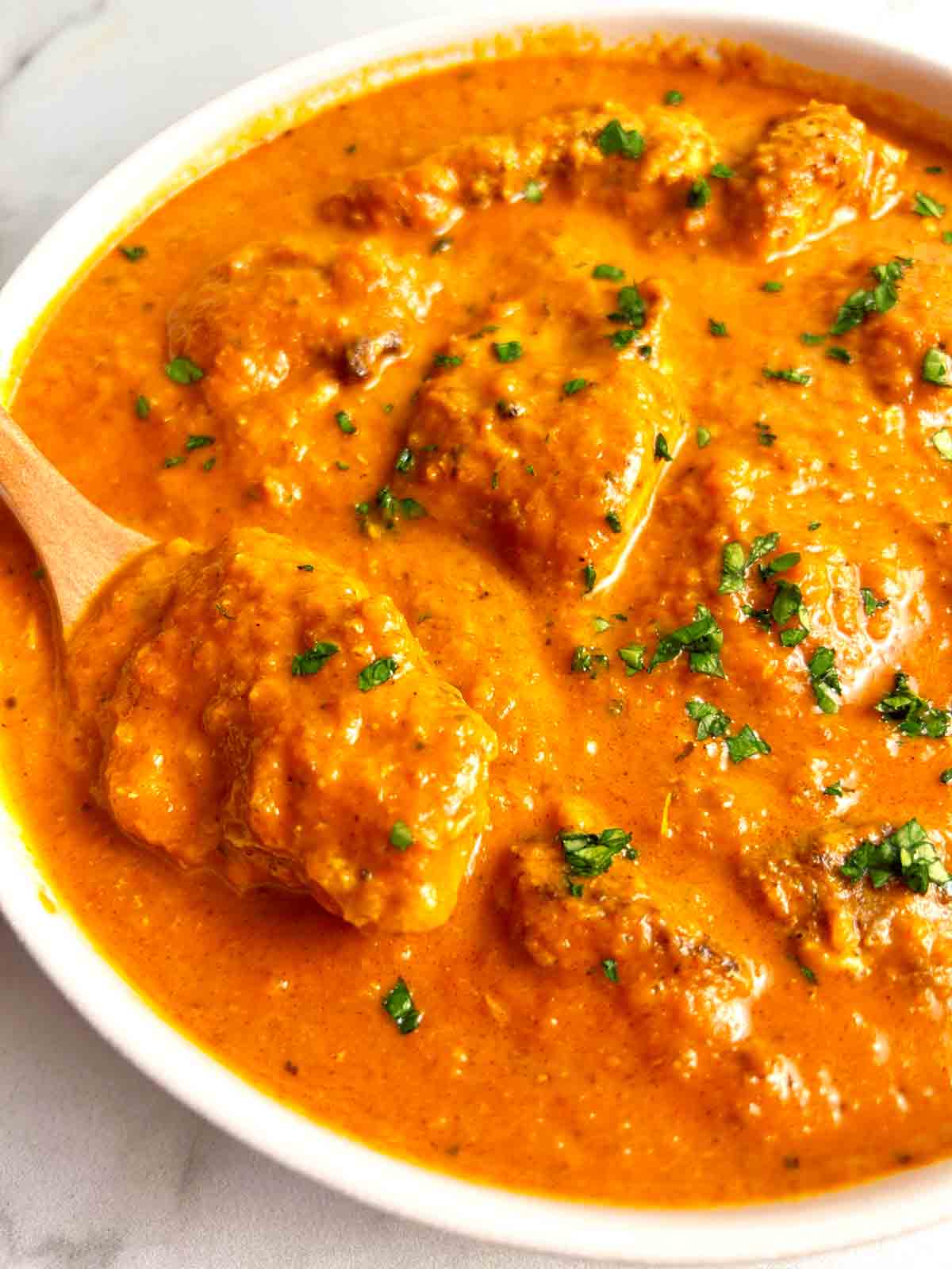 spoon lifting chicken from bowl of butter chicken.