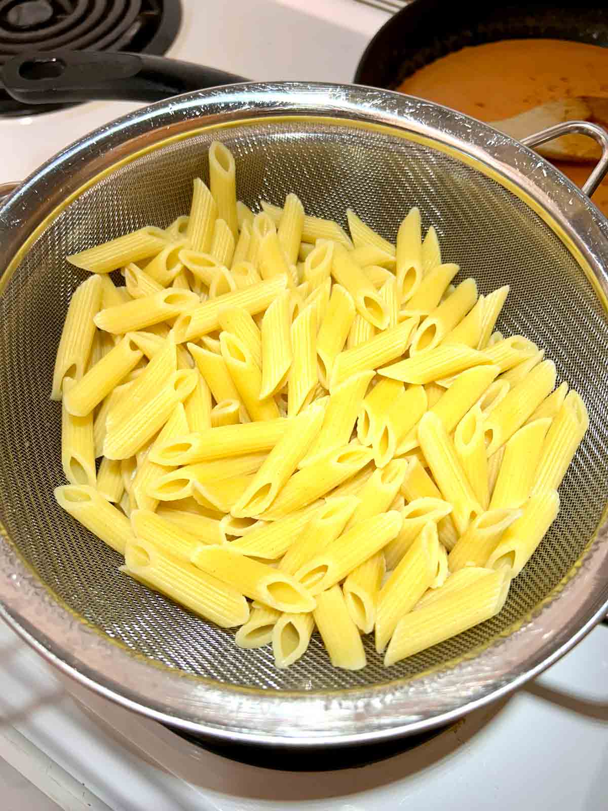 cooked penne being drained in colander.