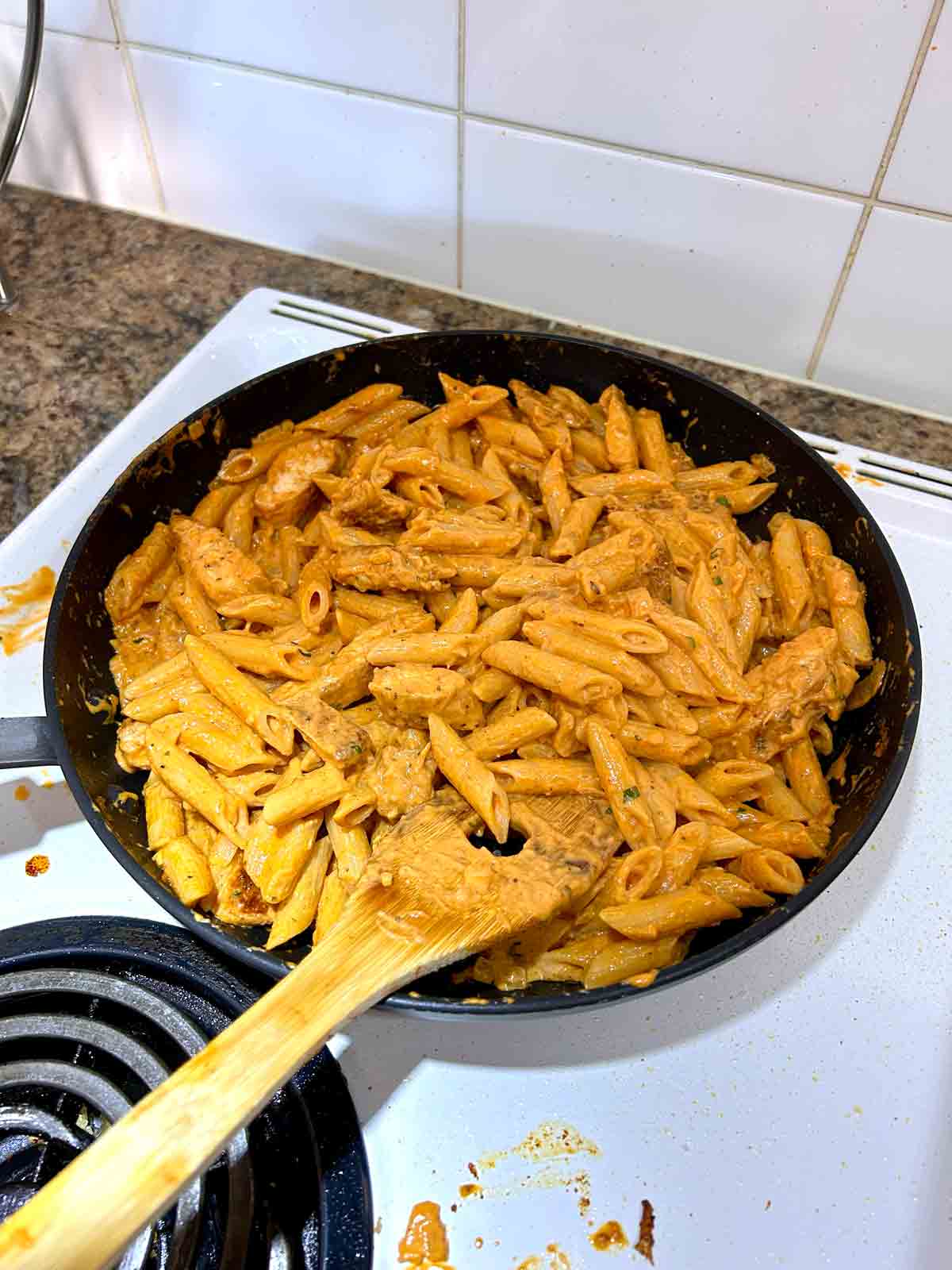 chicken and pasta being tossed with sauce in pan.