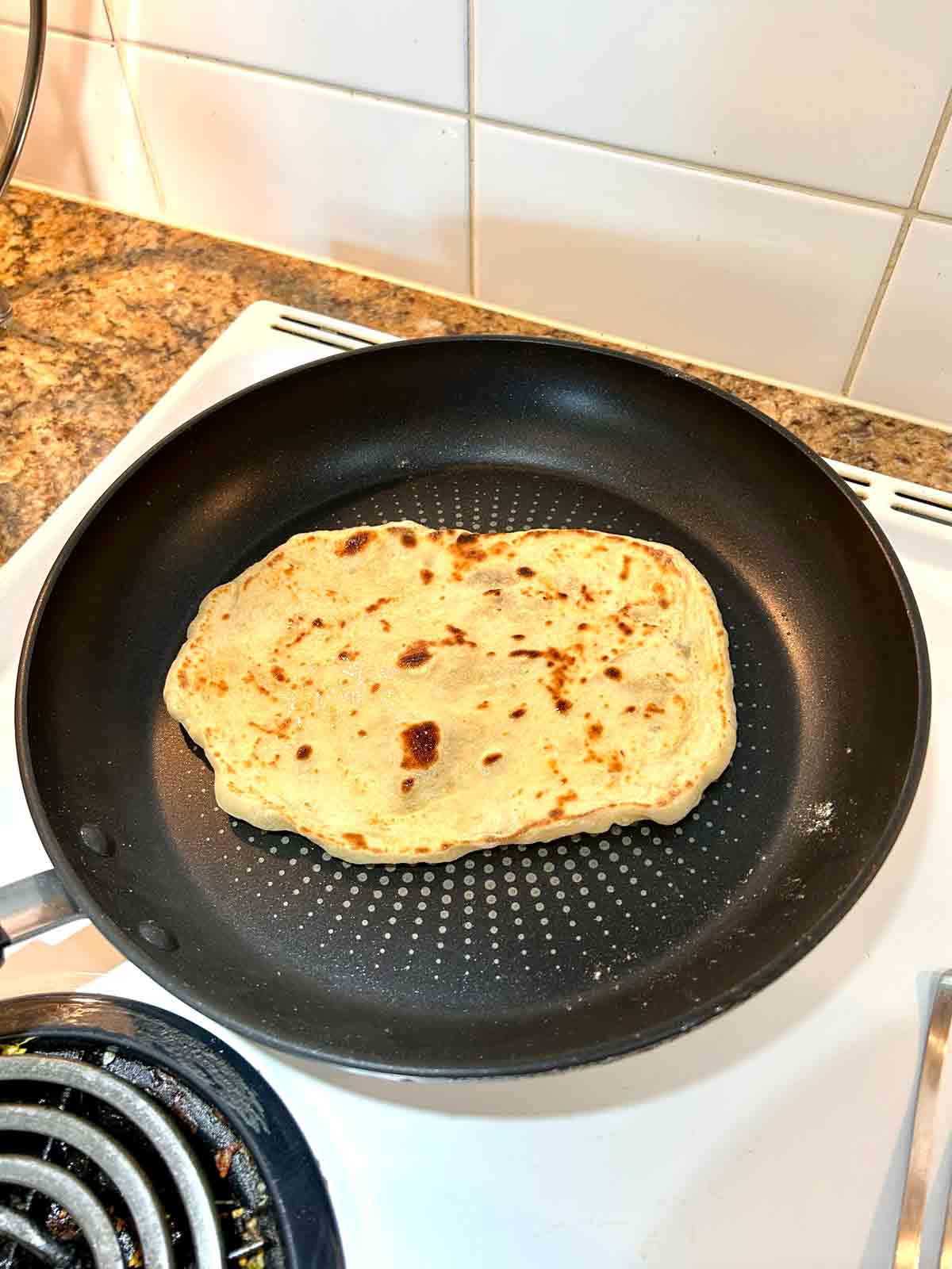 naan flipped in pan; outside is golden brown.
