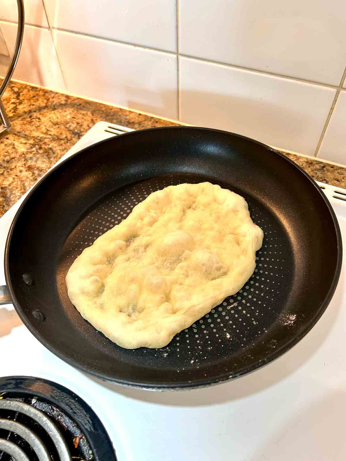 naan being cooked in pan; bubbles appearing in dough.