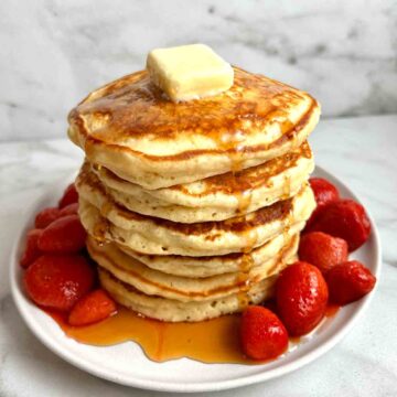 stack of pancakes with maple syrup and strawberry sauce.