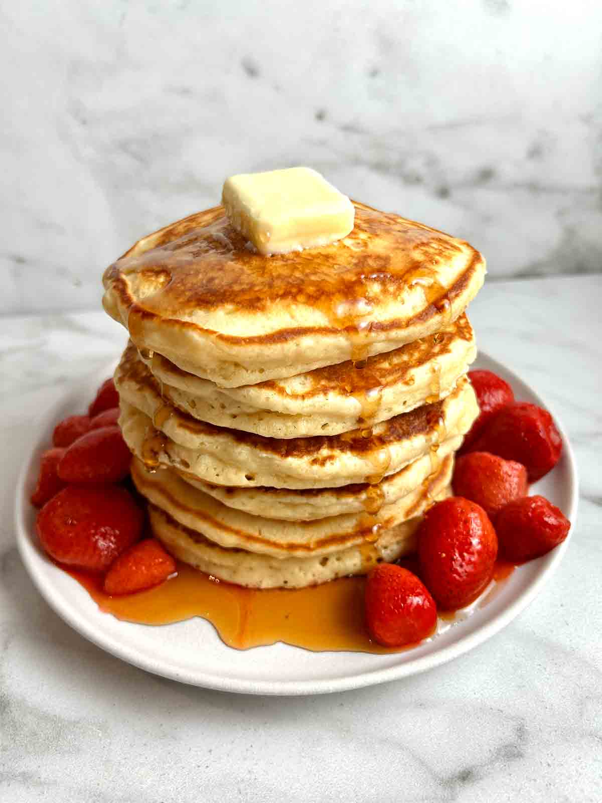 stack of pancakes with maple syrup and strawberry sauce.