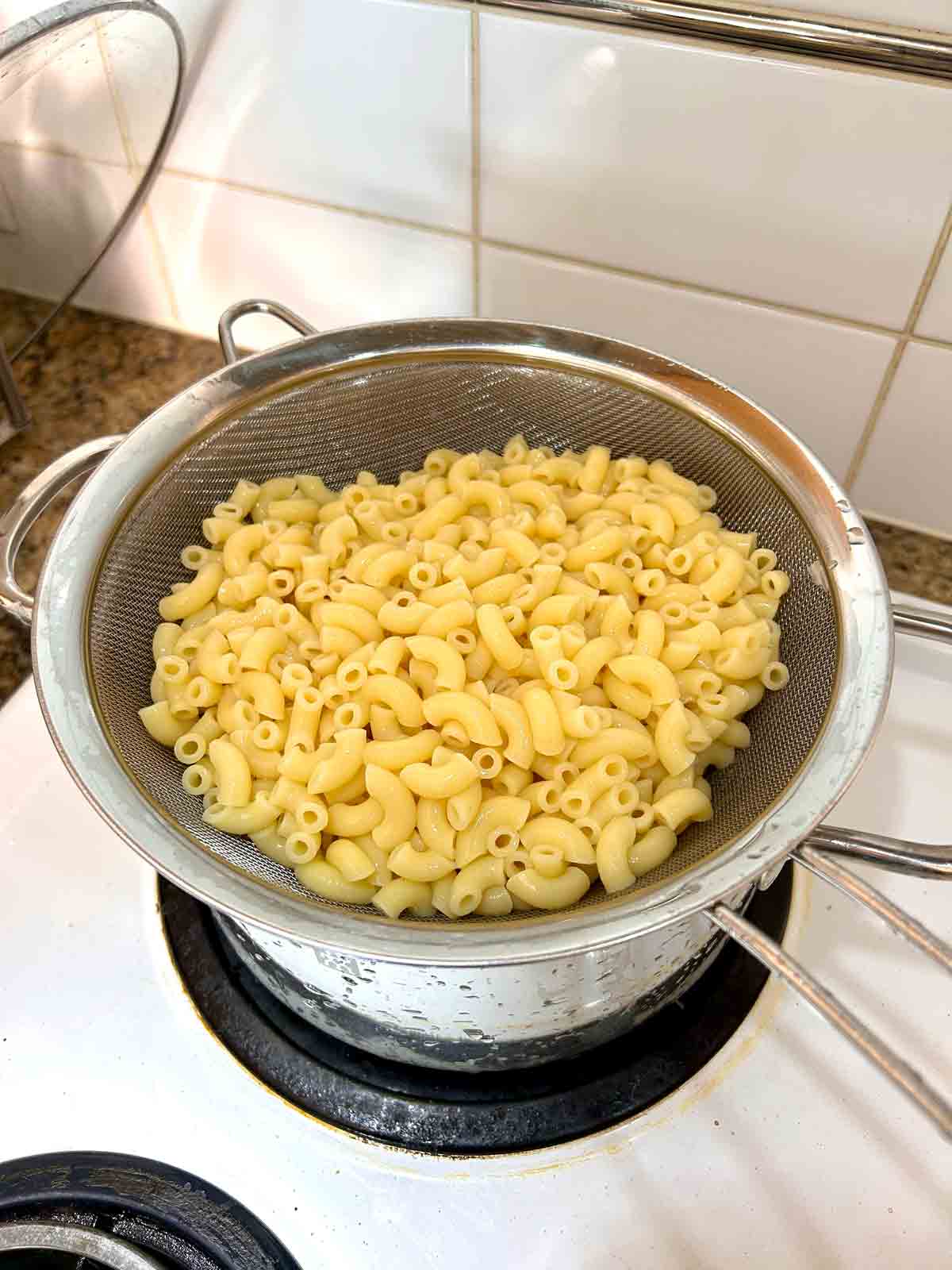 cooked macaroni draining over strainer.