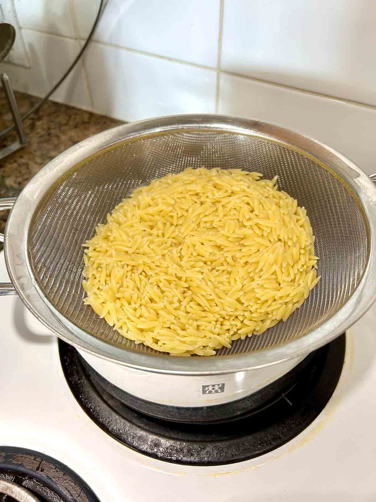 cooked orzo drained in strainer over pot.