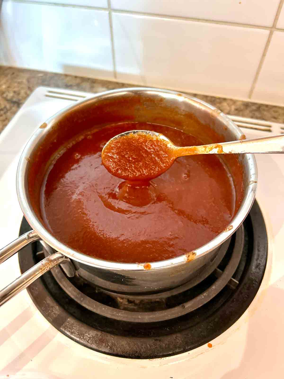 barbecue sauce being lifted out of saucepan with spoon.