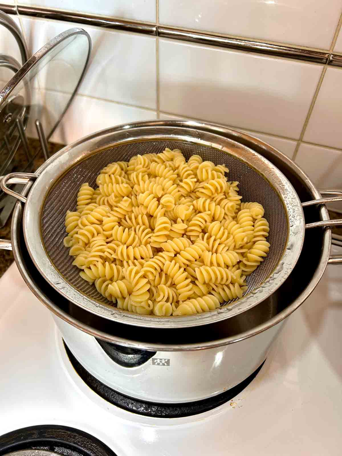 cooked rotini pasta being drained over colander.