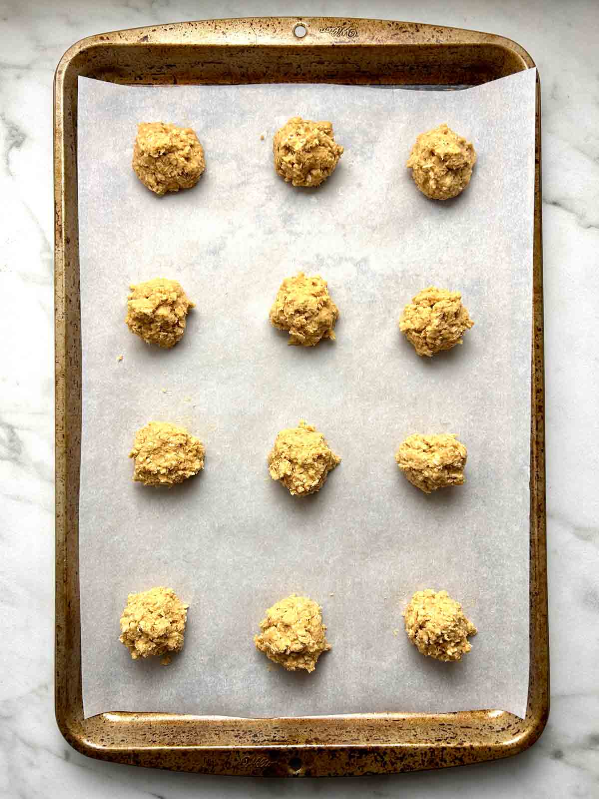 oatmeal cookie dough shaped into balls on parchment-lined baking sheet.