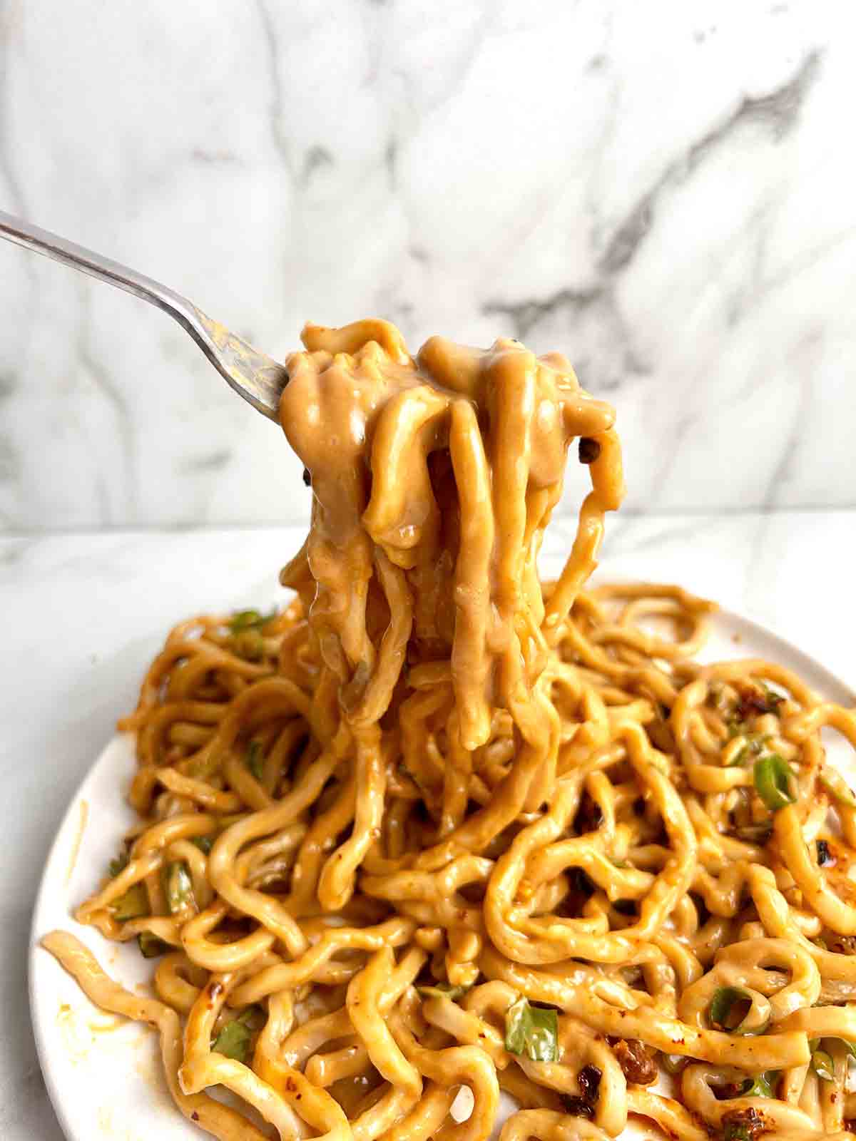 noodles covered in peanut sauce being lifted with fork from plate.