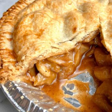 close up of apple pie with slice taken out still in pie pan.