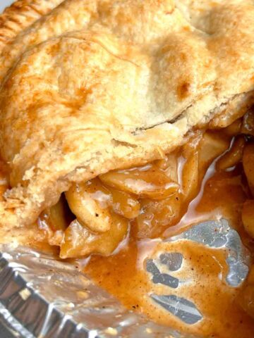 close up of apple pie with slice taken out still in pie pan.