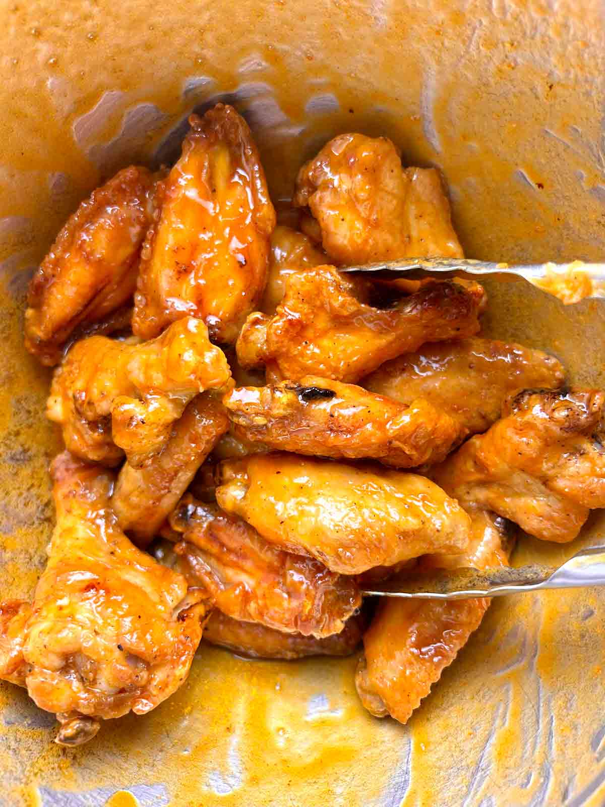 wings being tossed with buffalo sauce in large bowl.