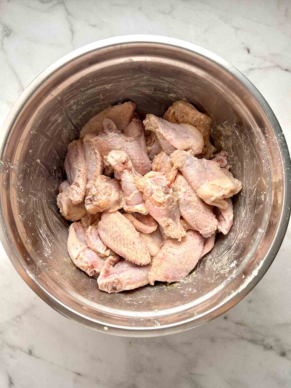 wings being mixed with seasonings in bowl.