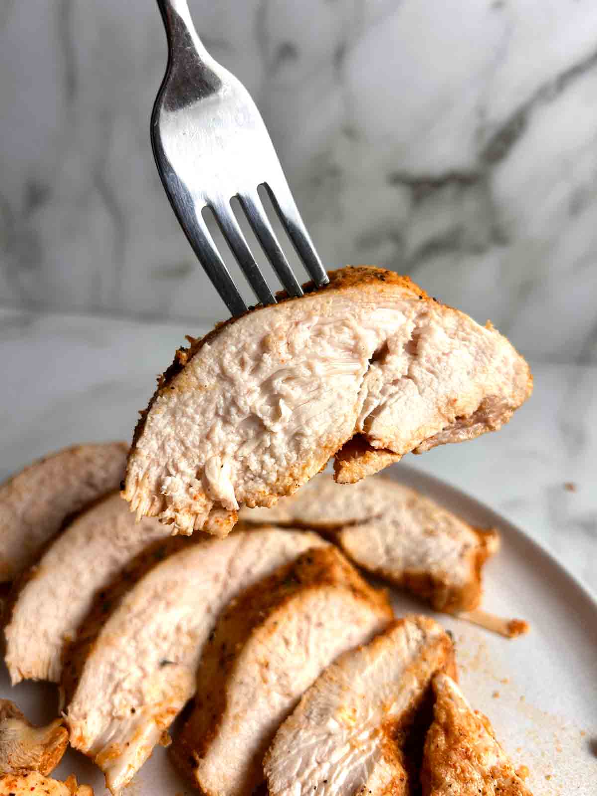 fork lifting sliced chicken breast to show juices inside.