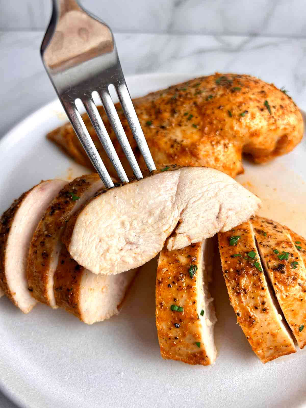 fork lifting sliced chicken breast to show juices inside.