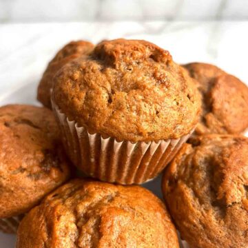 close up of banana muffin on top of other muffins on plate.