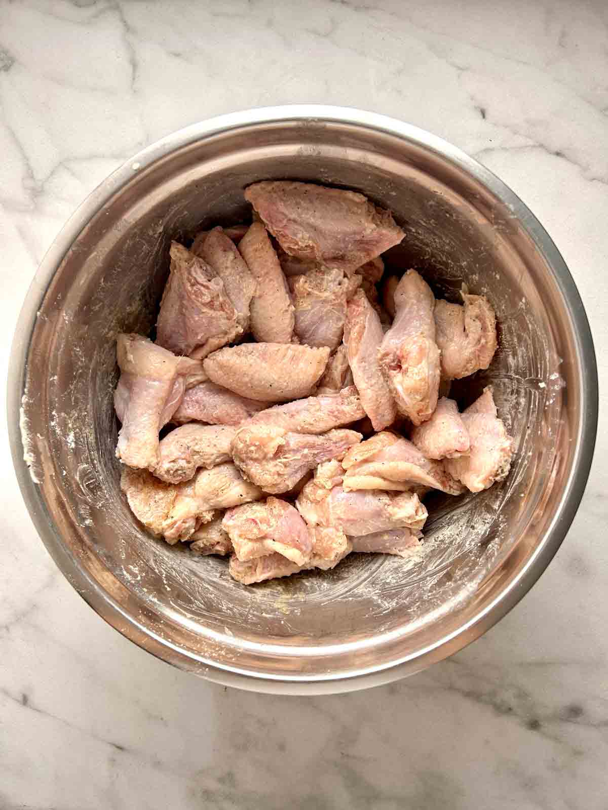 wings mixed with seasonings in bowl.