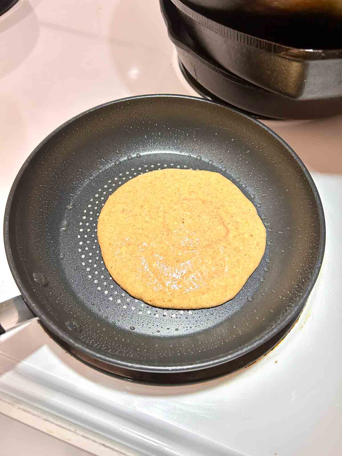 first side of pancake being cooked in pan.