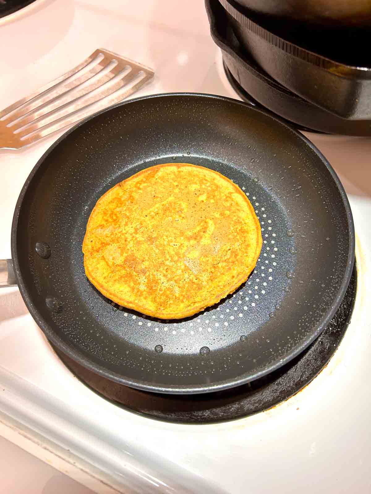 second side of pancake being cooked in pan.